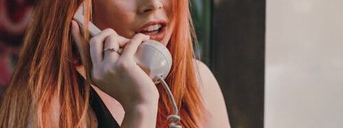 Free Stylish young redhead lady talking by vintage rotary telephone Stock Photo